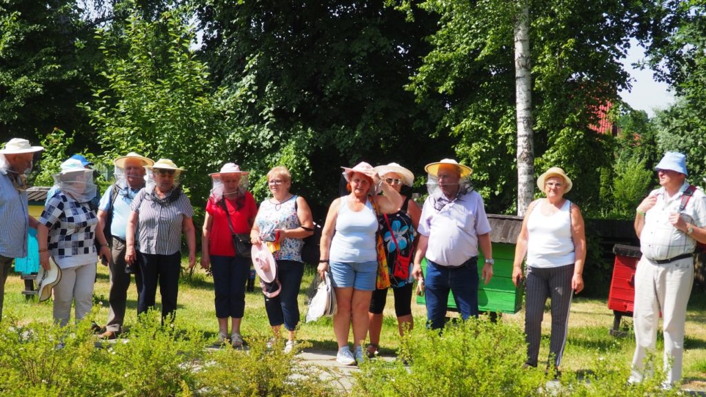 Uczestnicy projektu w ochronnych kapeluszach pszczelarskich zwiedzają pasiekę.